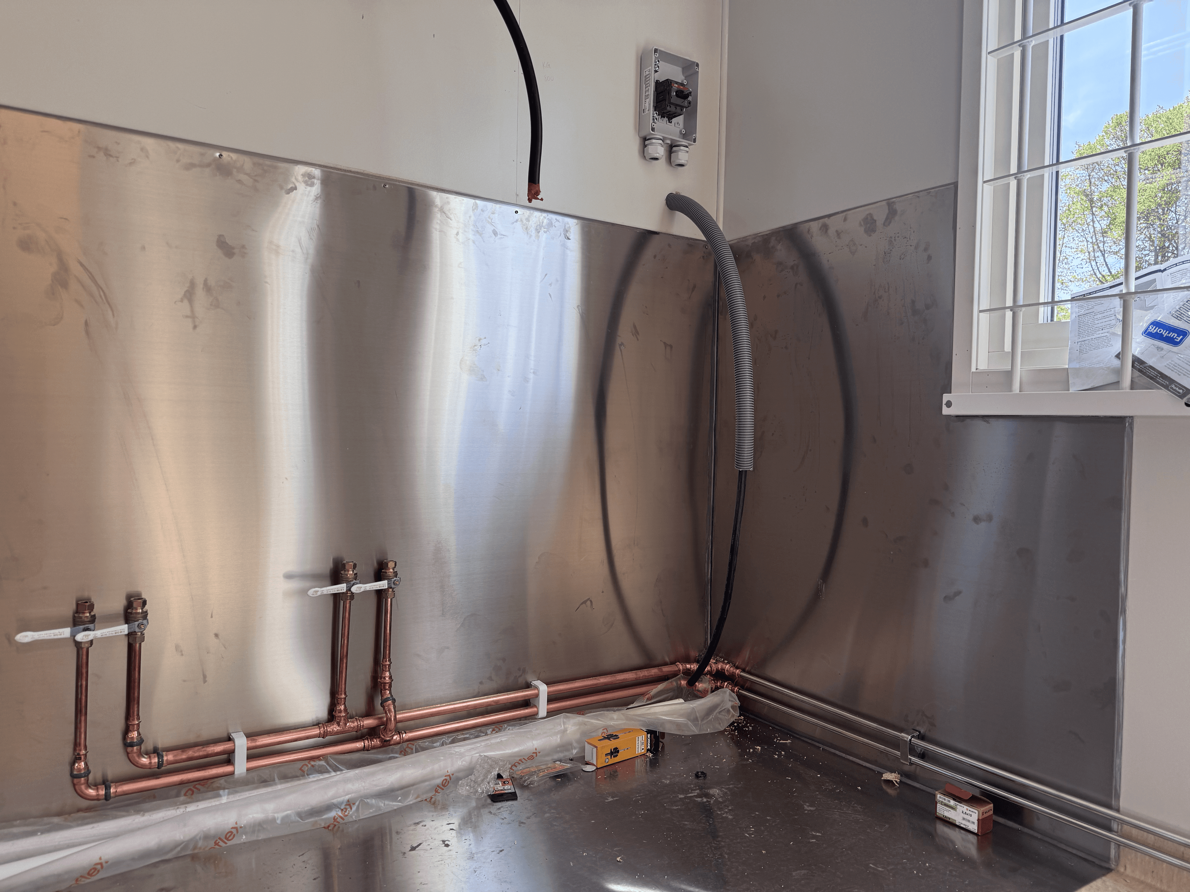 Gemensamt storkök med kopparrör, ventiler och rostfri stänkskydd i flerbostadshus.
